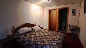 A bedroom with a bed, a nightstand, a lamp, a wooden door, and a television on the wall. - Hotel Cordillera Cabildo (Cabildo)