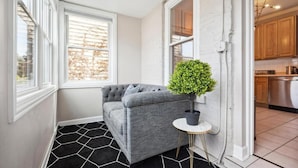 A corner room with a grey sofa, a small round table, a potted plant, and a black and white patterned rug. - Wrigleyville 2BR w/Parking, Firepit & Workspace for Remote Work (Chicago)