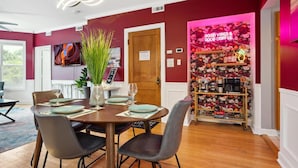 A dining area with a wooden table set for four, surrounded by chairs. A large vase with green plants is on the table. - Wrigleyville 2BR w/Parking, Firepit & Workspace for Remote Work (Chicago)