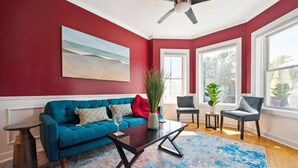 A living room with a teal sofa, a coffee table, and a large window with a view. - Wrigleyville 2BR w/Parking, Firepit & Workspace for Remote Work (Chicago)