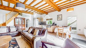 Zona d'estar àmplia amb un sofà de cuir, bigues de sostre de fusta i una cuina al fons.