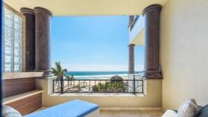 Een balkon met uitzicht op de oceaan, een rieten stoel, een tafeltje en een bank.