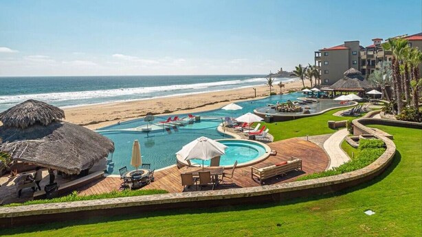 Een resort met een zwembad, uitzicht op het strand en rieten parasols.