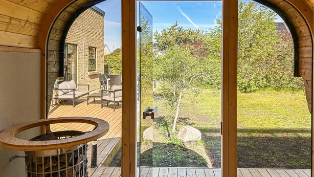 Een houten terras met tuinmeubilair, een vuurkuil en uitzicht op een stenen gebouw en tuin.