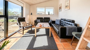 Een moderne woonkamer met een zwarte leren bank, een houten salontafel en een groot raam met uitzicht.