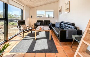 A modern living room with a black leather sofa, a wooden coffee table, and a large window providing a view of the outside.