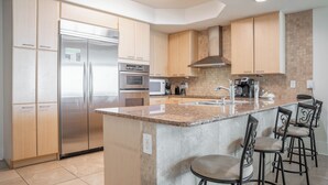 A modern kitchen with stainless steel appliances, wooden cabinets, a granite countertop, and bar stools.