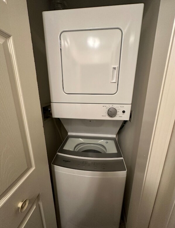 A compact, white laundry room with a front-loading washing machine and a dryer stacked above it.