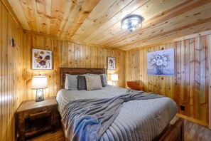 A wooden-paneled bedroom with a bed, two nightstands, and wall art.