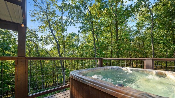 Un jacuzzi en una terraza de madera con vistas a un bosque.
