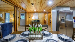 Un interior de madera con una mesa de comedor preparada para seis personas, un refrigerador y un techo de madera.