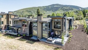 A modern multi-story house with large windows, a patio area, and a view of a forested mountain. - Abode at Moose Ridge, private hot tub, ski access, modern home (Park City)