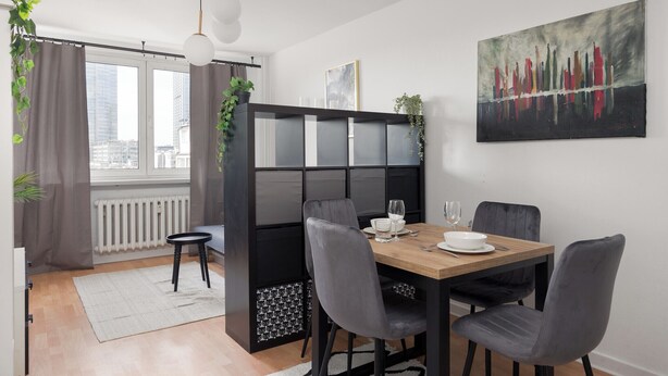 Et moderne spiseområde med et træbord, grå stole og en sort rumdeler.