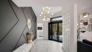 A modern interior with a geometric wall design, a white fur bench, a unique chandelier, and a view through a glass door. - Chic Palm Escape w/ Private Pool (Palm Desert)