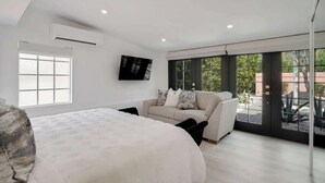 A modern bedroom with a large bed, a sofa, and a TV mounted on the wall. - Chic Palm Escape w/ Private Pool (Palm Desert)