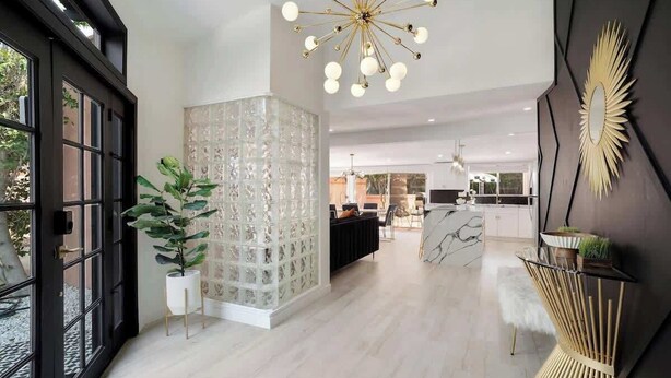 A modern interior with a glass partition, a central light fixture, and a kitchen in the background. - Chic Palm Escape w/ Private Pool (Palm Desert)