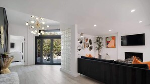A modern living room with a black sofa, a fireplace, and a TV mounted on the wall. - Chic Palm Escape w/ Private Pool (Palm Desert)