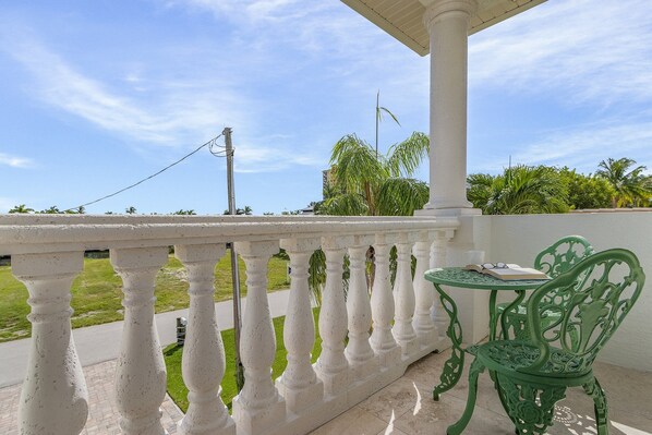 A balcony with a white balustrade, a green metal chair, and a table with a book and glasses.