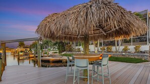 Une terrasse en bois avec un parasol en chaume, des sièges d’extérieur et une vue sur l’eau.