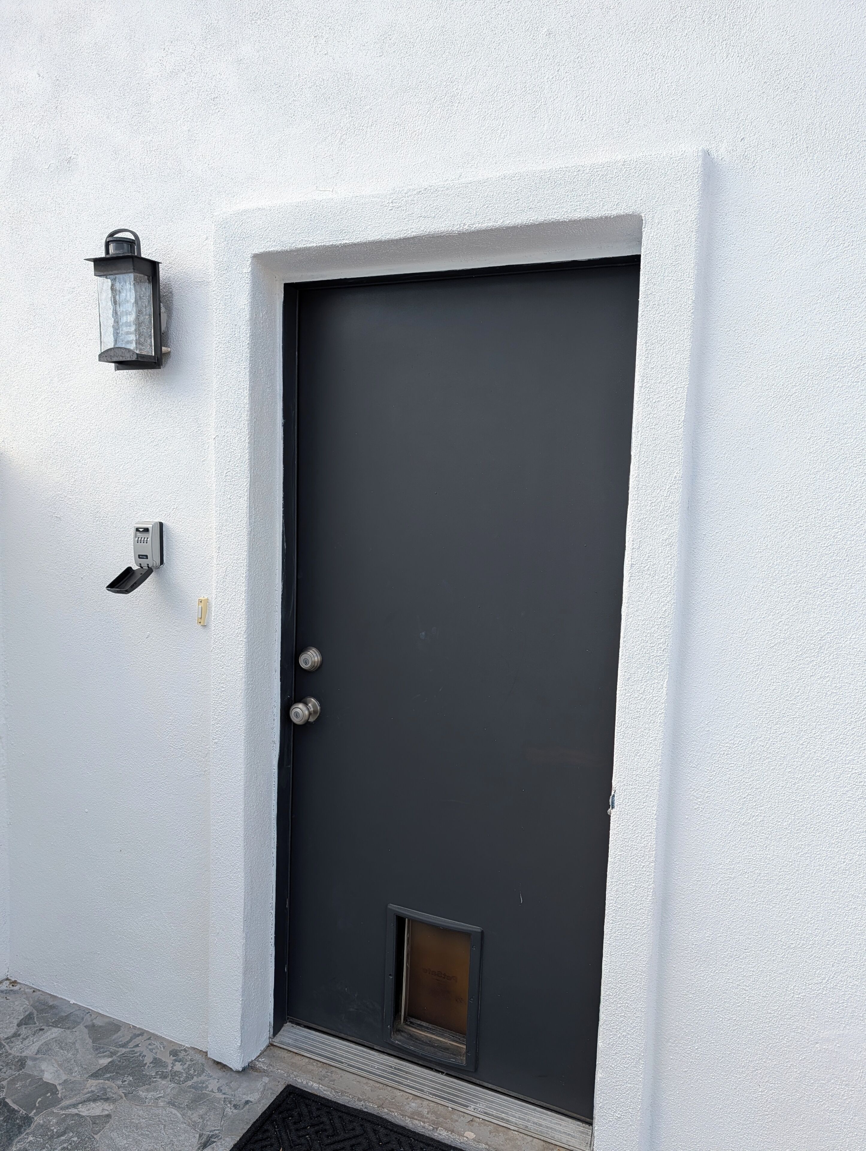 Eine dunkel gefärbte Tür mit kleinem Fenster, einer Wandleuchte und einem Sicherheitsschlüsselpad.