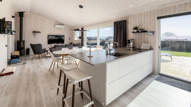 Une cuisine moderne dotée d’un grand îlot central, d’un coin repas avec des chaises blanches, d’un canapé et d’un téléviseur.