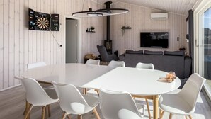 Un salon moderne avec une table blanche, des chaises blanches, un canapé gris, un téléviseur à écran plat et un jeu de fléchettes.