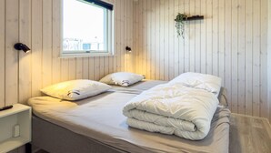 Un lit bien fait, avec des oreillers, une table de chevet, une fenêtre et une étagère fixée au mur, sur laquelle est posée une plante.