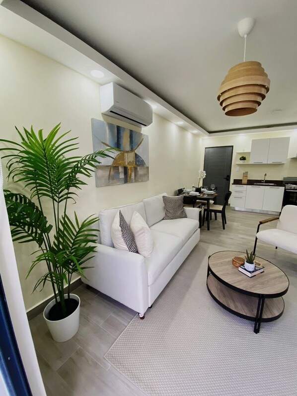 A modern living room with a white sofa, a coffee table, and a large potted plant. - Cozy 2-bedroom apartment in Punta Cana in a safe, Gated community with AC, WiFi. (Punta Cana)
