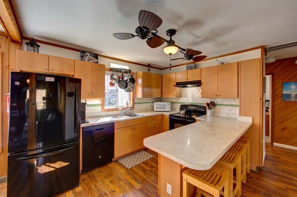 A compact kitchen with wooden cabinets, a black refrigerator, a microwave, and a stove. There is a wooden bar counter and stools.