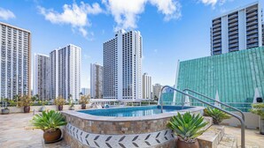 A rooftop pool with a stone mosaic border, surrounded by potted plants and modern high-rise buildings in the background. - Waikiki 1-bedroom condo with AC and wifi (Honolulu)