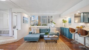A modern living room with a sectional sofa, a coffee table, and a view of the city through large windows. - Waikiki 1-bedroom condo with AC and wifi (Honolulu)