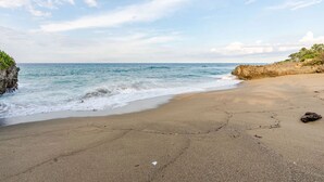 A beach with clear skies, calm waves, and rocky outcrops.
