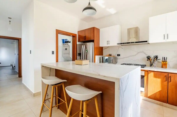 A modern kitchen with a marble countertop, wooden cabinets, and two bar stools. - Charming 2-bedroom villa Casa Blu in SOV, Puerto Plata Sosua (Puerto Plata Sosua)