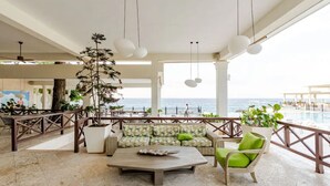 A spacious outdoor lounge area with a view of the sea, featuring a sofa, chairs, a coffee table, and potted plants.