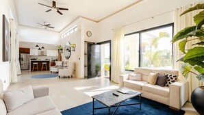 A spacious living room with a large window, a sofa, a coffee table, and a kitchen in the background.