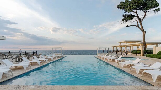 A pool with lounge chairs and a view of the sea.