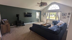 A living room with a dark green wall, a black fireplace, a blue sofa, a wooden coffee table, and a ceiling fan.