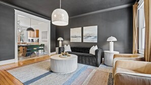 Una sala de estar moderna con una pared oscura, una mesa redonda, un sofá negro y un área de comedor visible a través de una puerta de cristal.