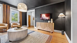 Una sala de estar moderna con una mesa redonda, dos sillones, un mueble de madera, un televisor y una lámpara de pie.