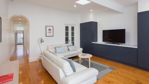 A modern living room with a sofa, a television, and dark cabinets. - North Adelaide - Row Cottage - “Monte” (North Adelaide)