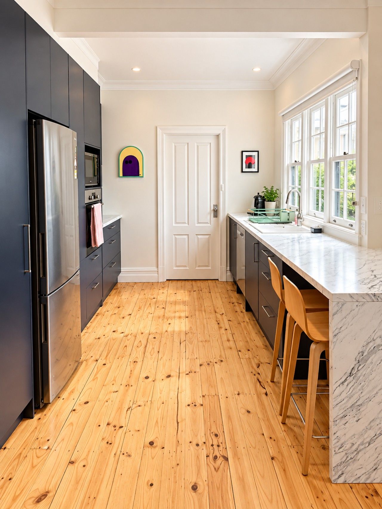 A modern kitchen with wooden flooring, stainless steel appliances, and a marble countertop.