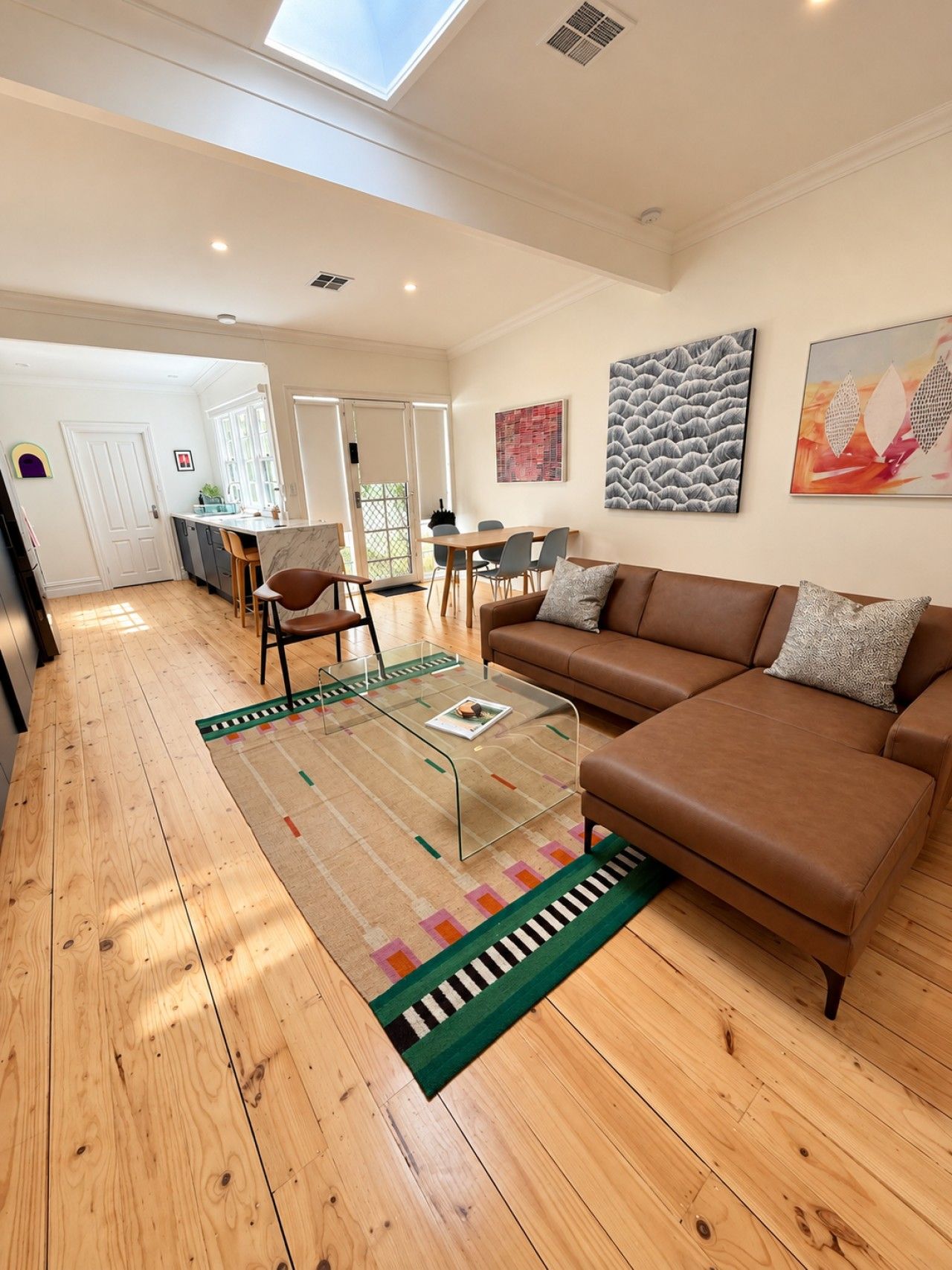 A spacious living area with a brown leather sofa, a glass coffee table, and a patterned rug.