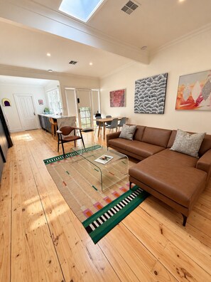 A spacious living area with a brown leather sofa, a glass coffee table, and a patterned rug.