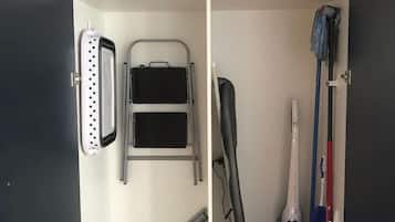 A storage unit with a laundry basket, ironing board, ironing board cover, ironing board stand, and a mop.