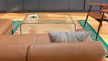 A modern living room with a leather sofa, a glass coffee table, a television on a stand, and grey cabinets.