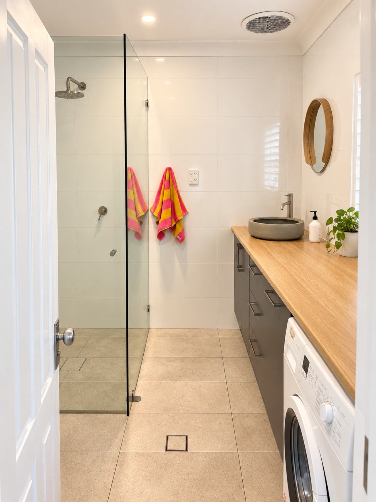 A modern bathroom with a glass shower enclosure, a sink with a round basin, a mirror, and a washing machine.