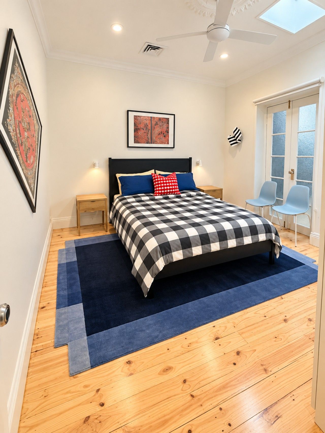 A bedroom with a bed, a ceiling fan, a skylight, a door with frosted glass, and a wall-mounted picture.