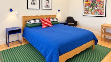 A bedroom with a wooden bed, green striped rug, two wall-mounted lamps, a ceiling fan, and two framed pictures.