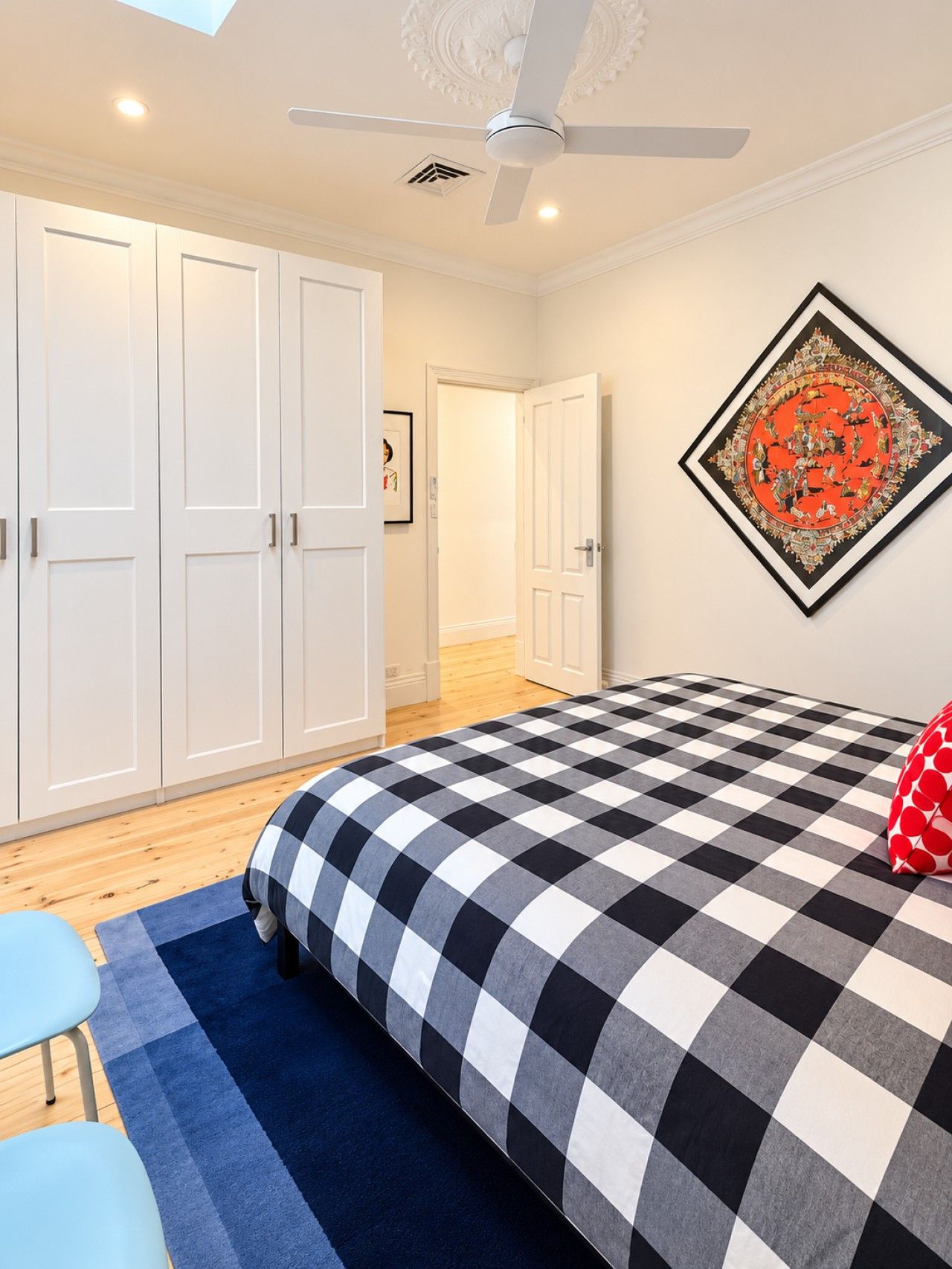 A bedroom with a checkered bedspread, a ceiling fan, and a large artwork on the wall.