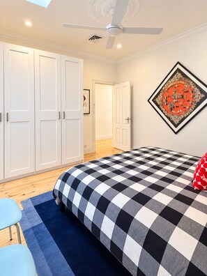 A bedroom with a checkered bedspread, a ceiling fan, and a large artwork on the wall.